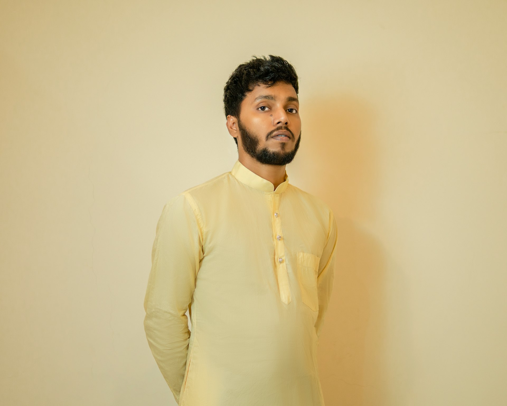 a man standing in front of a wall wearing a yellow shirt